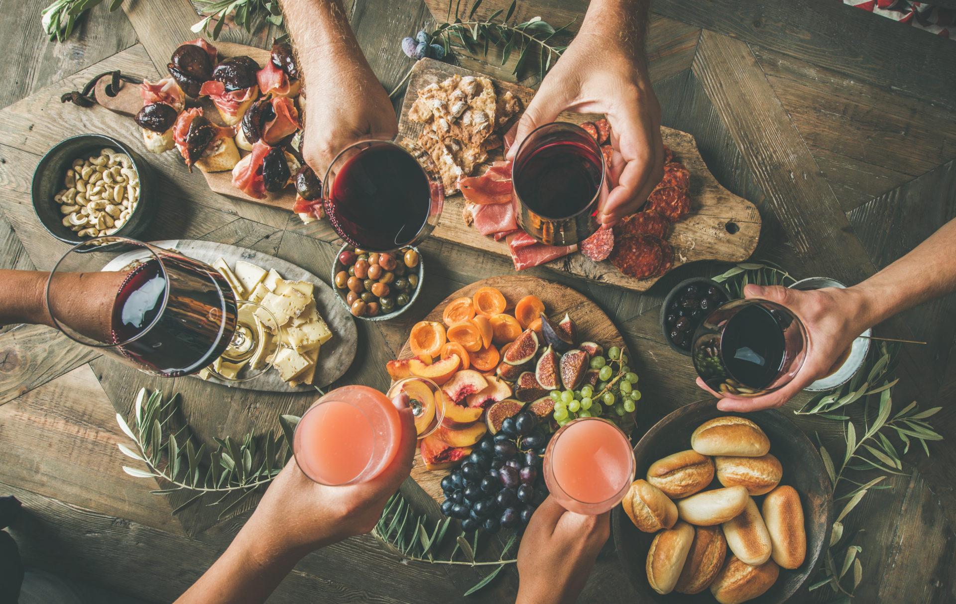 Flat-lay of friends eating and drinking together. Top view of people having party, gathering, dinner together sitting at wooden rustic table set with wine snacks and fingerfoods. Hands with glasses